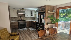 Una cocina con estufa, horno, refrigerador y armarios de madera. Hay una mesa de comedor con sillas y un sillón amarillo.