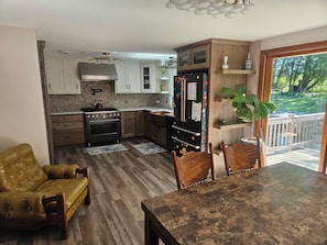 Une cuisine équipée d’une cuisinière, d’un four, d’un réfrigérateur et de meubles de rangement en bois. On y trouve une table à manger avec des chaises et un fauteuil jaune.
