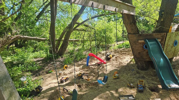 Un parque infantil con columpios, un tobogán y vehículos de juguete.