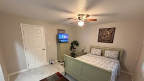 A bedroom with a bed, a ceiling fan, a TV, a dresser, and a door. - Cozy 1-bedroom house in fantastic Cocoa with air conditioning (Cocoa)