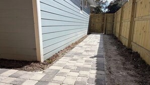 A paved pathway leading to a wooden gate, flanked by a light-colored building and a wooden fence. - Cozy 1-bedroom house in fantastic Cocoa with air conditioning (Cocoa)