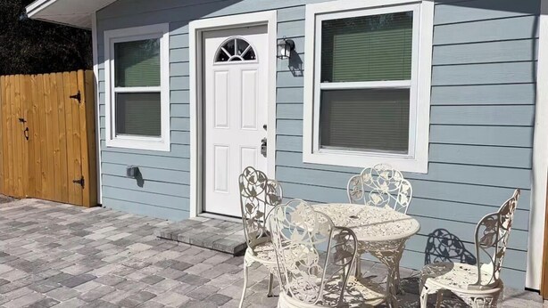 A house with a front door, two windows, a patio with a table and chairs, and a wooden fence. - Cozy 1-bedroom house in fantastic Cocoa with air conditioning (Cocoa)