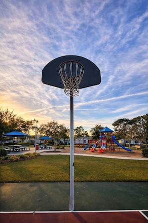 Ein Basketballfeld mit Korb, umgeben von einem Spielplatz mit Rutschen und Schaukeln.