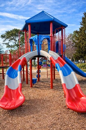 Ein Spielplatz mit zwei Rutschen, einer blauen Dachkonstruktion und roten und weißen Geländern.