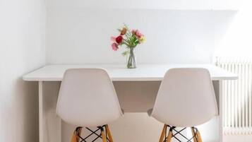 A white desk with two chairs, a vase with flowers, and a radiator in the background.