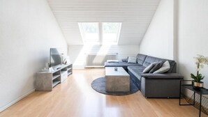 Une chambre de style loft moderne, avec un plafond en pente, des fenêtres de toit, un canapé gris, une petite table basse et un téléviseur posé sur un meuble.
