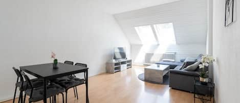 A modern loft apartment with a dining area, a living room with a sofa and coffee table, and a TV.