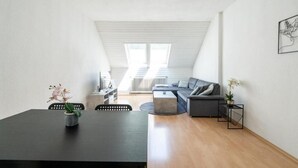 Un appartement moderne de style «loft», comprenant un coin repas, un canapé et offrant une vue sur le ciel grâce à une verrière.