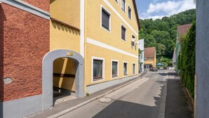 Une rue étroite bordée de bâtiments jaunes, un mur en briques rouges et, au loin, une colline verdoyante.