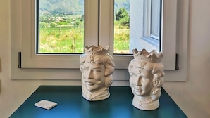 Una habitación con ventana que da a un paisaje, un aparador decorativo con diseño estampado y dos esculturas blancas en el alféizar.