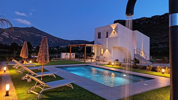 Una casa moderna con piscina, mobiliario exterior y montañas al fondo.