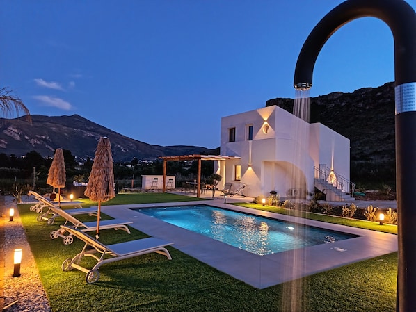 A modern house with a swimming pool, outdoor seating, and a mountain backdrop.