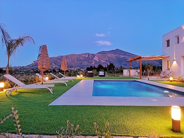 Une piscine avec des chaises longues, une pergola et une vue sur la montagne.