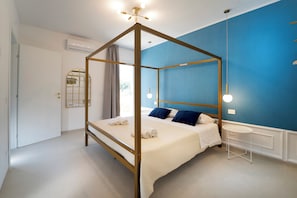 Un lit à baldaquin avec un couvre-lit blanc et des coussins bleus, une petite table ronde et un mur d’accent bleu.