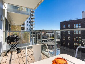 Un balcón con una mesa, sillas, un cochecito de bebé y vistas de los edificios circundantes.