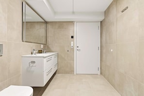 Un bany modern amb un tocador blanc, un mirall gran i una porta.