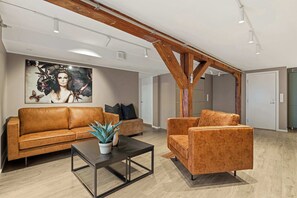 Un vaste espace de vie comprenant un canapé en cuir marron, un fauteuil assorti, une table basse et un grand tableau accroché au mur.