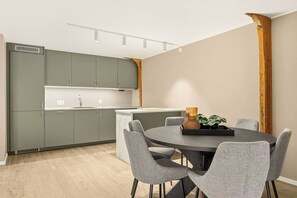 A modern kitchen with grey cabinets, a round dining table, and grey upholstered chairs. - 2BR Seaside Apartment - SKB17-R2 (Bergen)