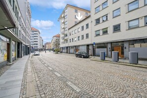 Una strada acciottolata fiancheggiata da edifici a più piani, un’auto parcheggiata e un pedone.