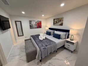 Een moderne slaapkamer met een bed, nachtkastjes, een bankje en kunstwerken aan de muur.