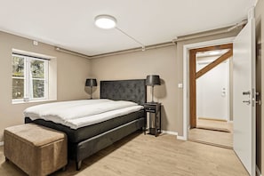 Un dormitorio con una cama, lámparas de noche, suelo de madera, una ventana y una puerta.