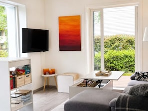 Una sala de estar moderna con televisor, un cuadro, una ventana con vistas a la vegetación y un sofá.