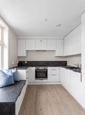 Una cocina moderna con armarios blancos, horno empotrado y encimera oscura.