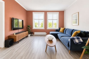 Un salon moderne avec un téléviseur à écran plat, un canapé bleu, une table basse blanche et un meuble en bois.