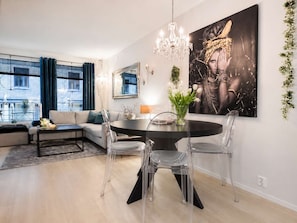 Una sala de estar moderna con una mesa de comedor redonda, sillas transparentes, una araña y un cuadro abstracto grande.