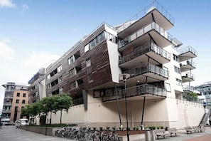 Un edificio residencial de varios pisos con balcones, una zona de aparcamiento para bicicletas y cielo despejado.