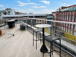 Una terraza en la azotea con mesa y sillas, vistas de edificios circundantes y cielo despejado.