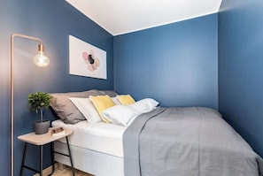 Une chambre à coucher avec un lit, une table de chevet avec une lampe, une plante en pot et une œuvre d’art murale.