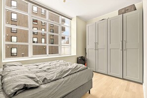 Een slaapkamer met een bed, een raam met uitzicht op een gebouw en grijze kledingkasten.