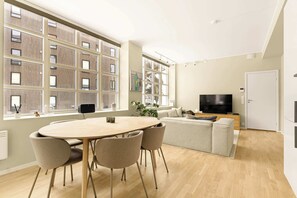 Een moderne woonkamer met een ronde tafel, stoelen, een bank, een televisie en grote ramen.