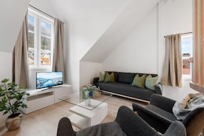 En moderne stue med et fladskærms-tv, en sofa med puder, et sofabord og en potteplante.