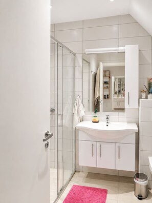 Een moderne badkamer met een glazen douchecabine, een witte wastafel en een spiegel erboven.