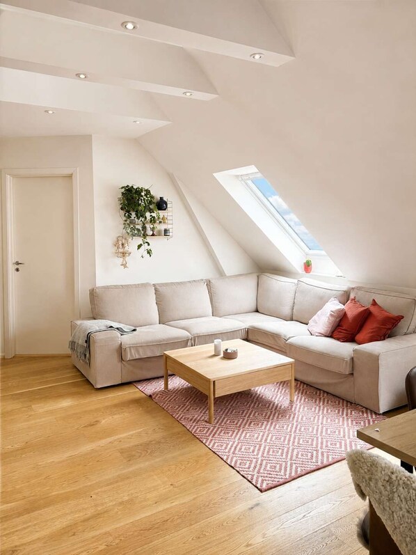 Een moderne loft met een groot dakvenster, een hoekbank, een houten salontafel en een vloerkleed met een patroon.