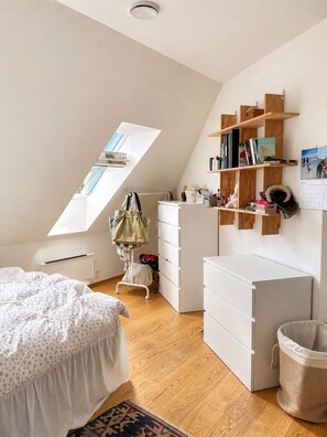 Een slaapkamer met een schuine plafond, een bed, een bureau, een kledingkast en een plank met boeken en persoonlijke spullen.