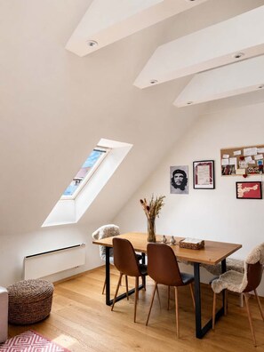 Een eethoek met een houten tafel, stoelen, een vaas met gedroogde bloemen en een prikbord met diverse spullen erop.