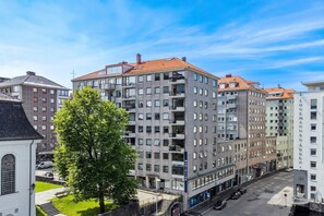 En bygning med flere etager, altaner, parkeringsplads og et træ i forgrunden.