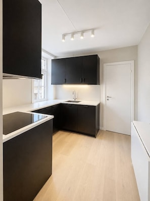 Une cuisine moderne avec des meubles de couleur sombre, un plan de travail blanc et une cuisinière intégrée.