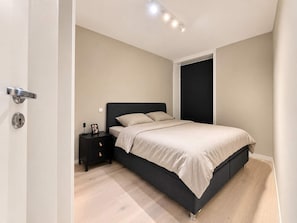Une chambre à coucher avec un lit, une table de chevet, une porte et un luminaire.