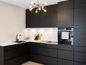 Una cocina moderna con armarios oscuros, encimera blanca, horno integrado y una lámpara de techo original.