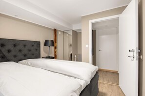 Habitación de hotel con una cama grande, una mesita de noche con lámpara, un armario y una puerta que da a otra habitación.