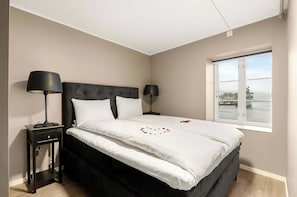 Quarto com cama, duas mesas de cabeceira com luminárias, janela com vista e decoração em formato de coração na cama.