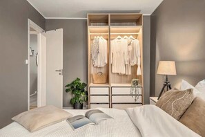 Un dormitorio con una cama, una mesita de noche con lámpara, un armario y una planta en maceta.