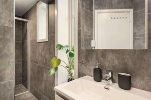 Un baño moderno con ducha, lavabo con espejo y una planta.