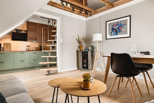 Una cocina moderna con armarios verdes, una escalera de madera y un comedor con mesa y sillas.