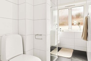 A bathroom with white tiles, a toilet, a shower area, a window with a view, and a towel hanging on the wall. - MK38 2BR Cozy Apartment Bergen (Bergen)