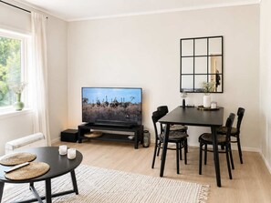 A modern living room with a flat-screen TV, a dining table with chairs, a black-framed mirror, and a window with curtains. - MK38 2BR Cozy Apartment Bergen (Bergen)